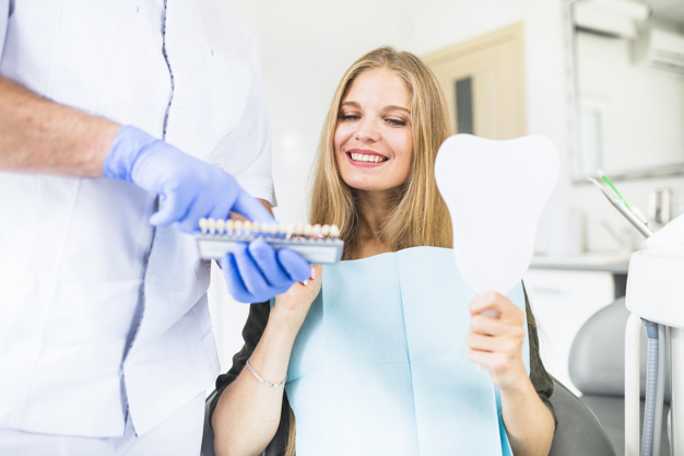 happy-female-patient-choosing-color-tone-of-her-teeth-using-shade-guide_23-2147862058